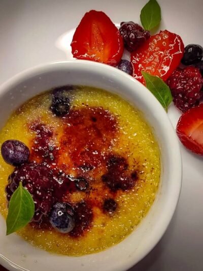 Creme brûlée com crosta caramelizada e frutas vermelhas frescas.